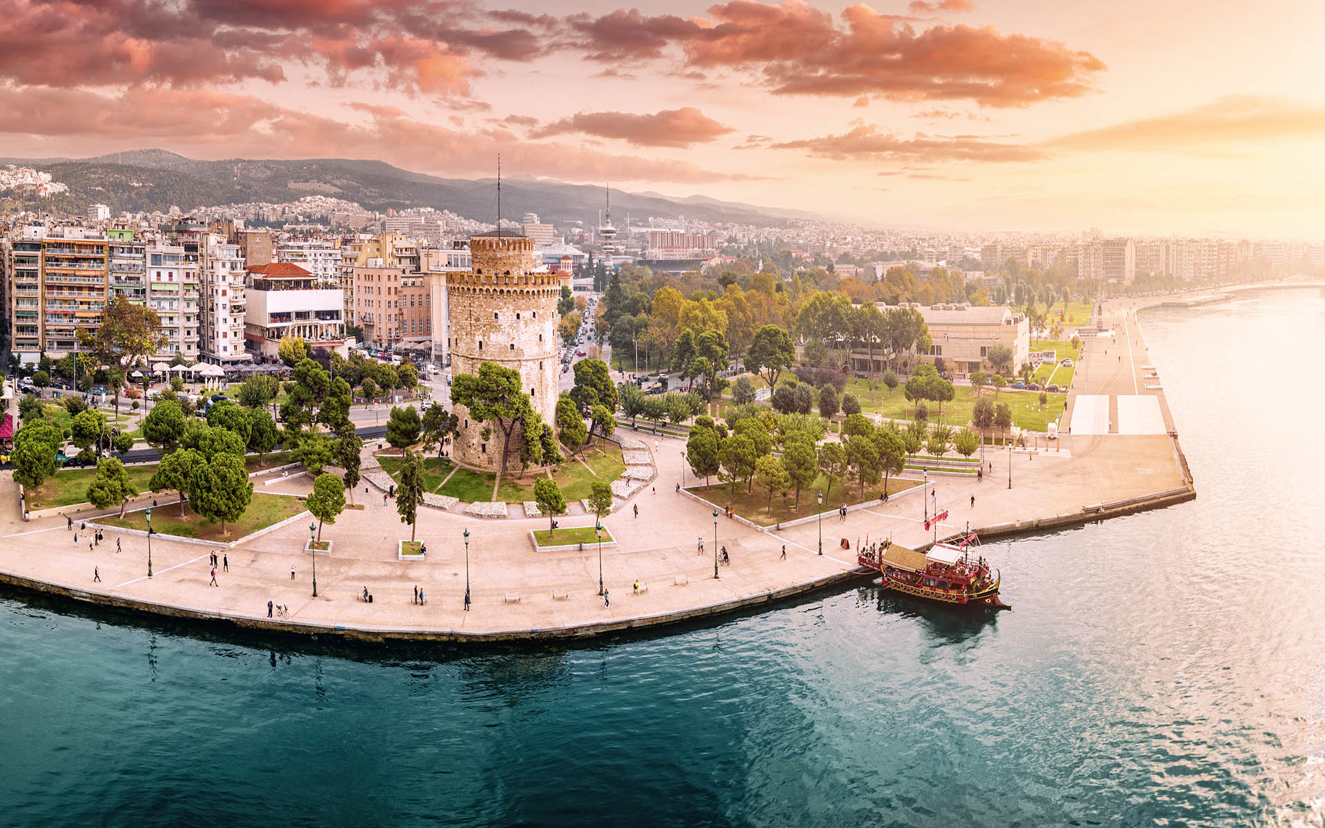 Aerial panoramic view of the main symbol of Thessaloniki city - the White Tower with boat tour ship at the pier. Concept of travel landmarks in Greece and urban development.