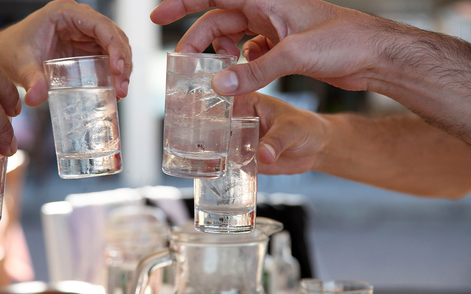 Close up of the hands of three guys clinking their glasses of a traditional greek drink tsipouro together