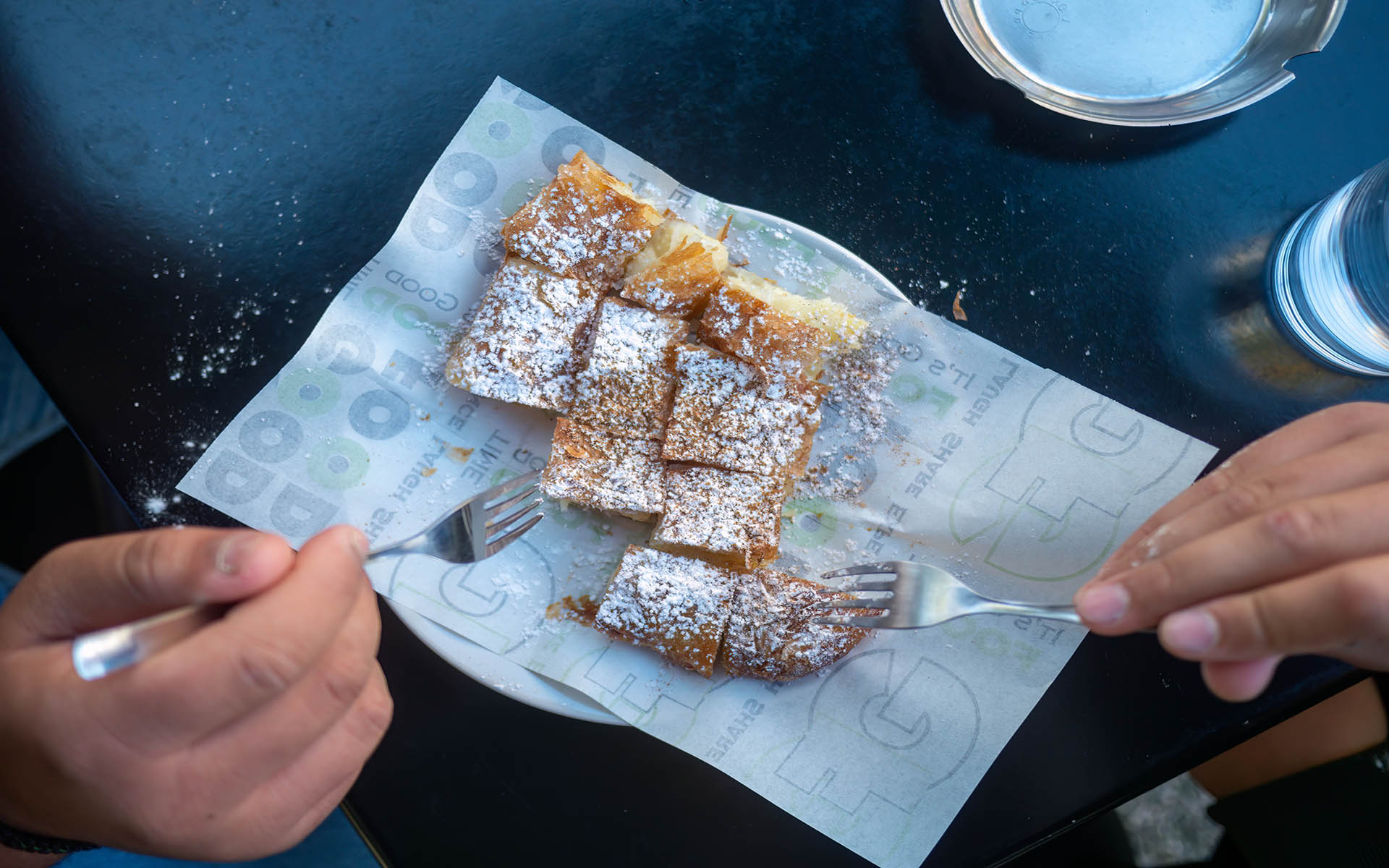 Closeup of hands eating traditional Greek bougatsa, a sweet cream pie pastry with filo dough, dusted with powdered sugar and cinnamon. Popular breakfast or snack from Thessaloniki and Serres, Greece.